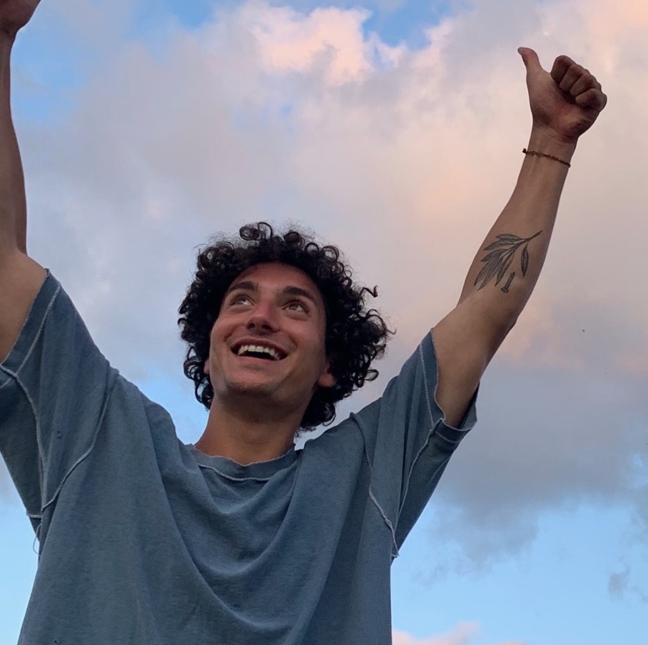 Headshot of writer and student Levi Baruch; hands in the air, smiling with a dramatic look into the sky