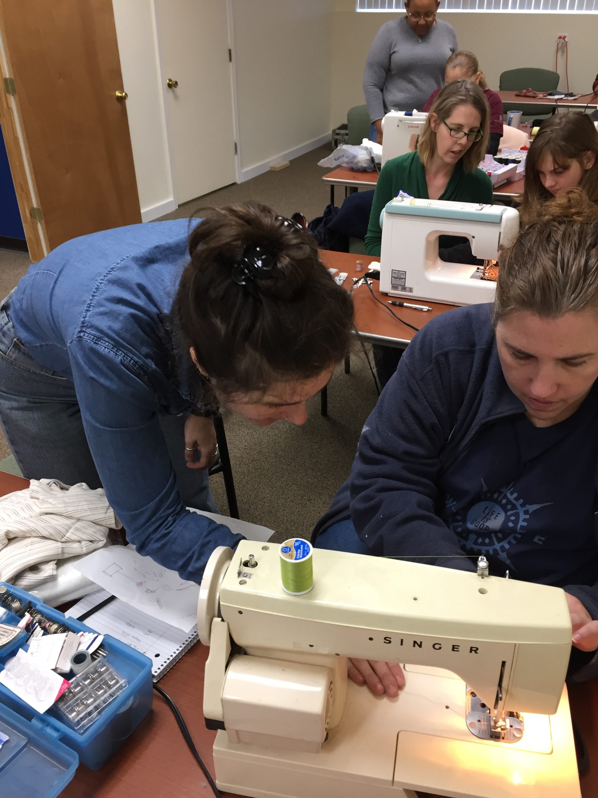 Podcast guest Erin Kiewel assisting a textile student at the sewing machine in 2020