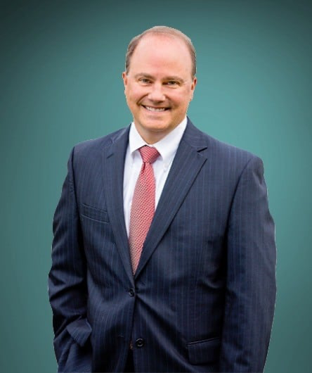 Headshot in full color of Gardner (MA) City Solicitor John Flick, in a blue suit with light red tie. 