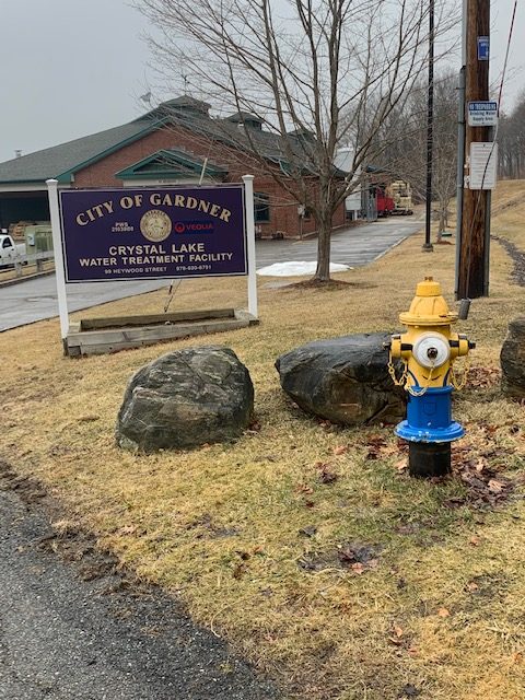 Exterior full color image of the painted blue and yellow fire hydrant and blue sign outside of the Dept. of Water Management in Gardner, MA.