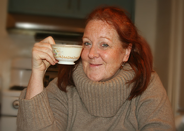 Headshot of Artist Claire Daly after being interviewed for the Jazz Room. She is wearing a brown sweater and holds a white porcelian coffee cup in her right hand, held up to her face.