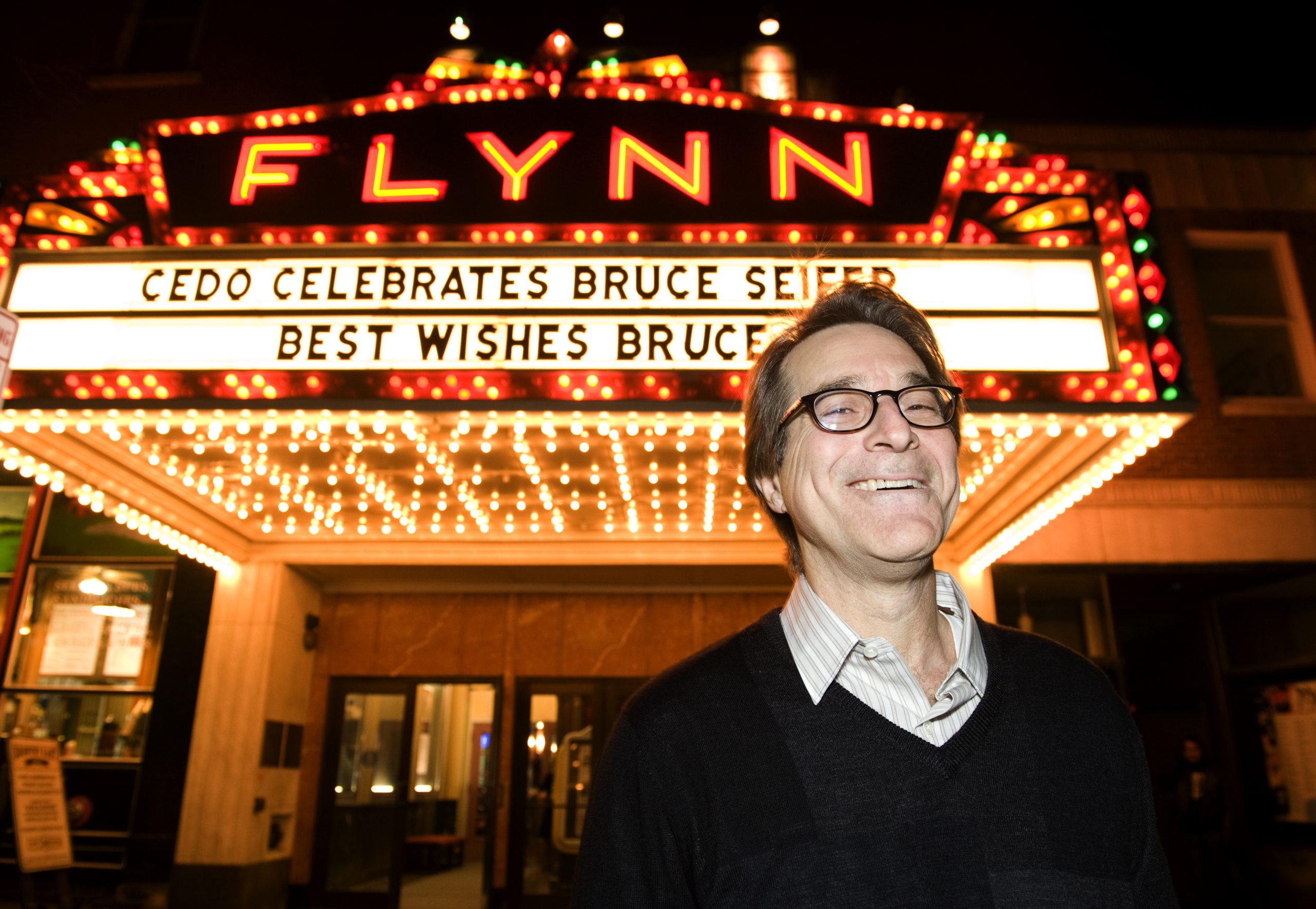 Famed Economic Development Professional Bruce Siefer in front of the marquee for the Flynn Theatre, downtown Burlington, VT. Full color photo taken at night. 