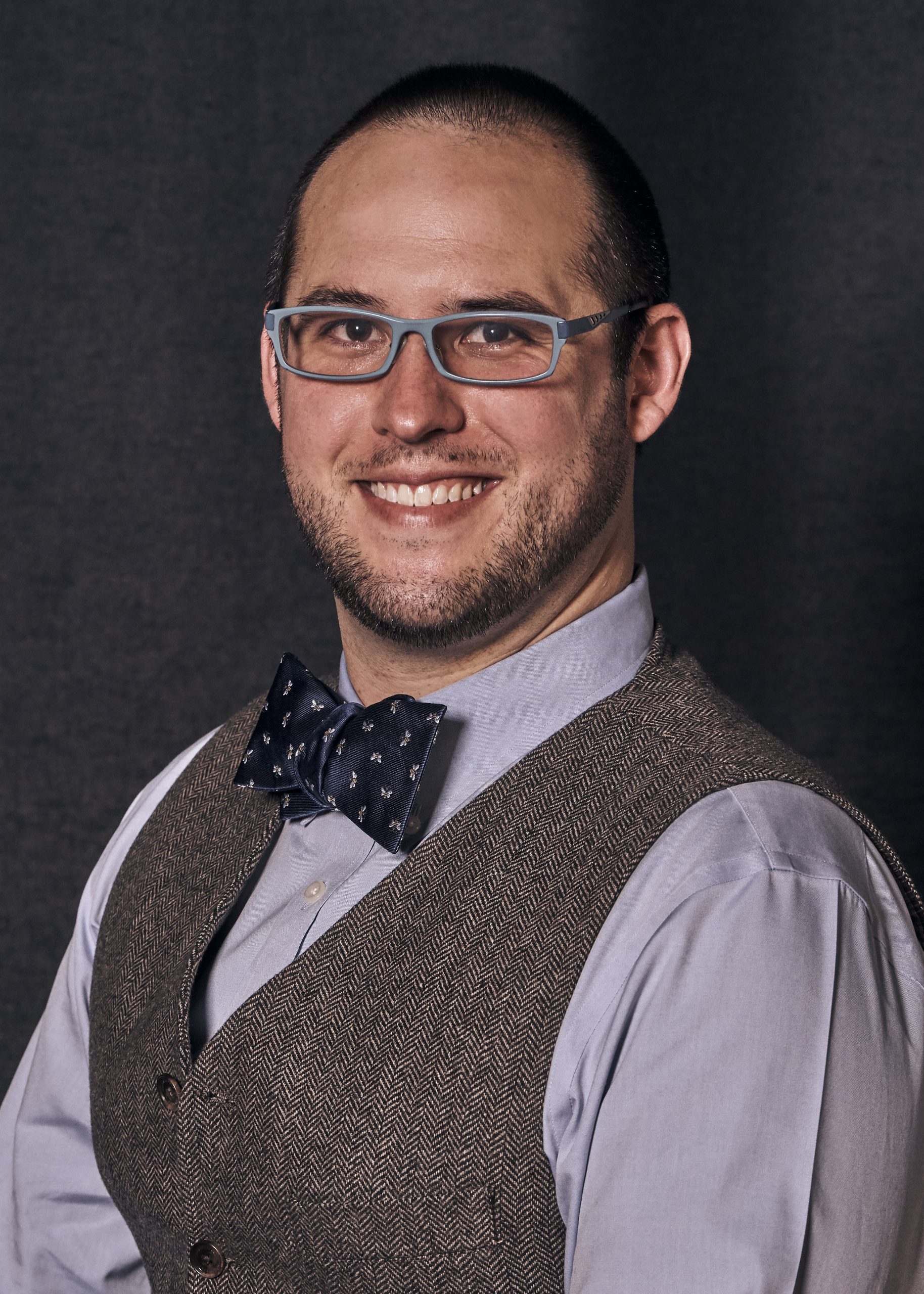 Full Color headshot of Deputy Executive Director of Black River Innovation Center Chris Magliolo.  We is wearing a light blue shirt, navy blue gold polka-dotted bow tie and sporting a wool grey suit vest.