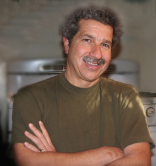 Full Color Headshot of Jazz Trumpeter Mark Morganelli, in brown sandy T-shirt, smiling, salt and pepper hair with mustache. 