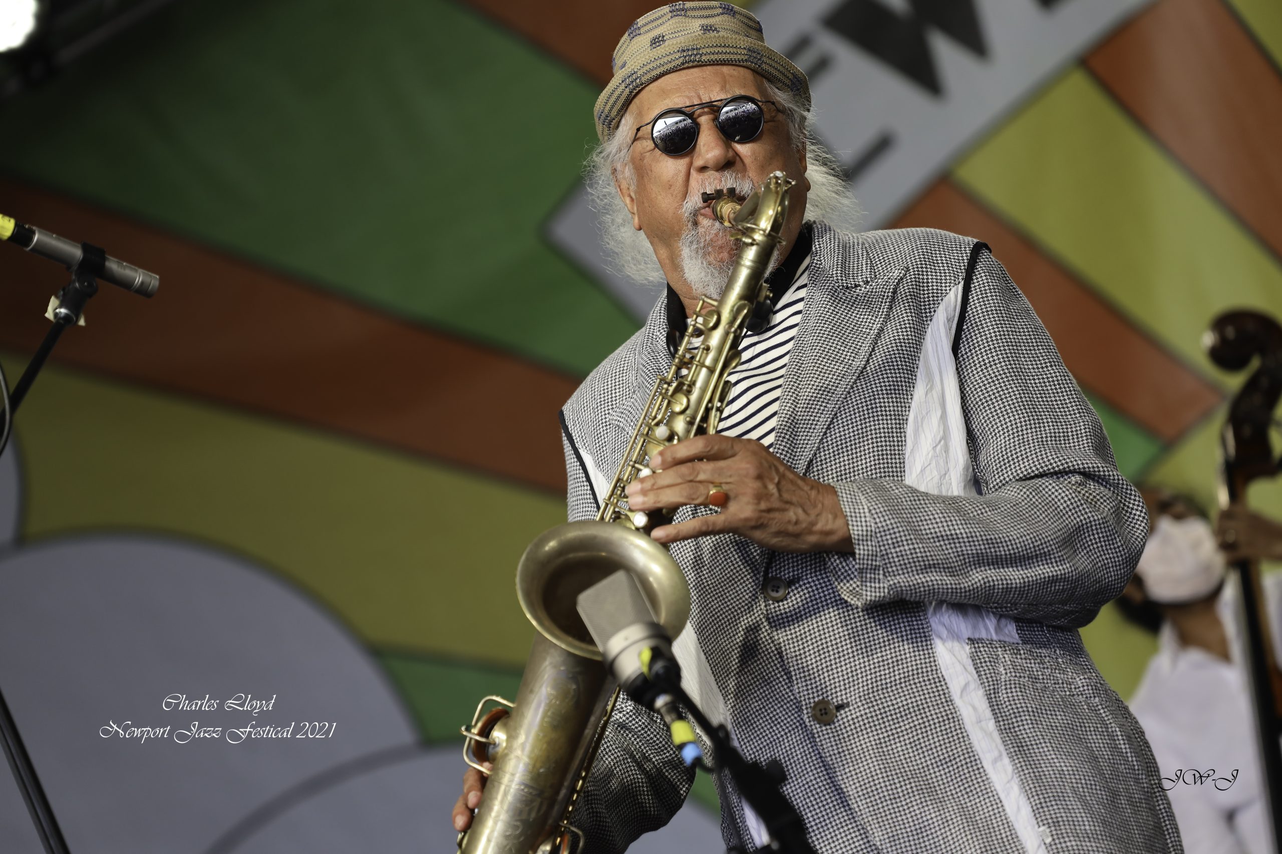 Saxophonist Charles Lloyd performing on tenor saxophone, colorful stage display behind him at the Newport Jazz Festival