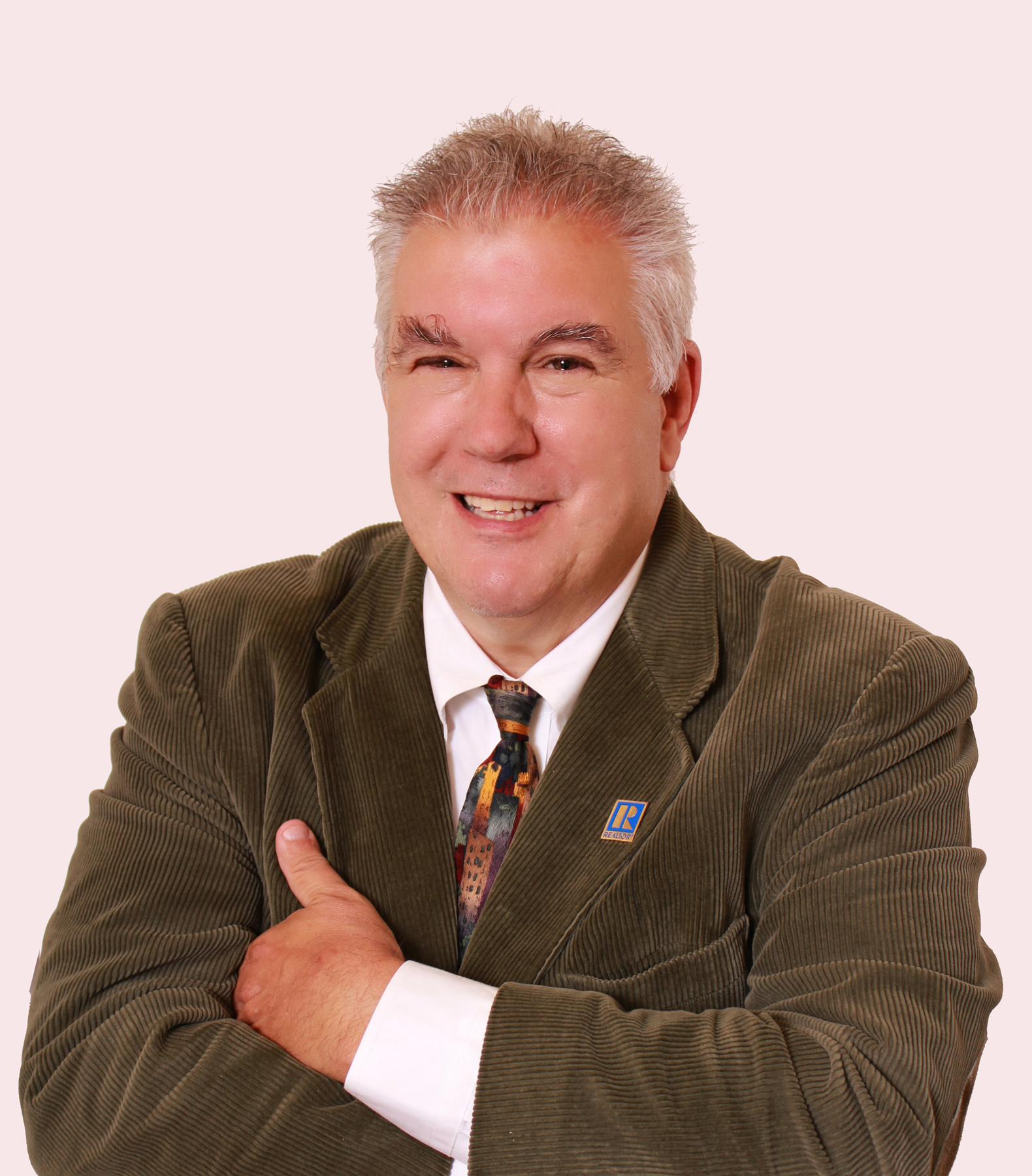 Full color headshot of Rail Trails advocate and real estate professional Craig Della Penna in a green sport coat, smiling, colorful patterned tie and arms crossed. 